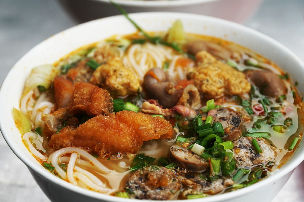 A bowl of snakehead fish noodle soup with vermicelli, herbs, and tomatoes in Moc Chau